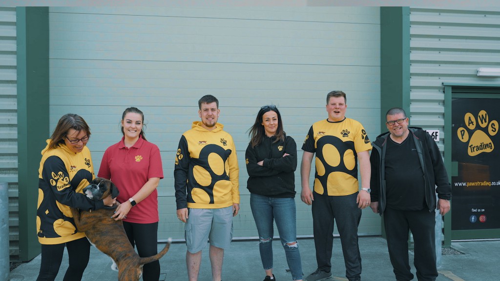 The Paws Trading team stand in front of their warehouse as a large boxer dog jumps up on Paula