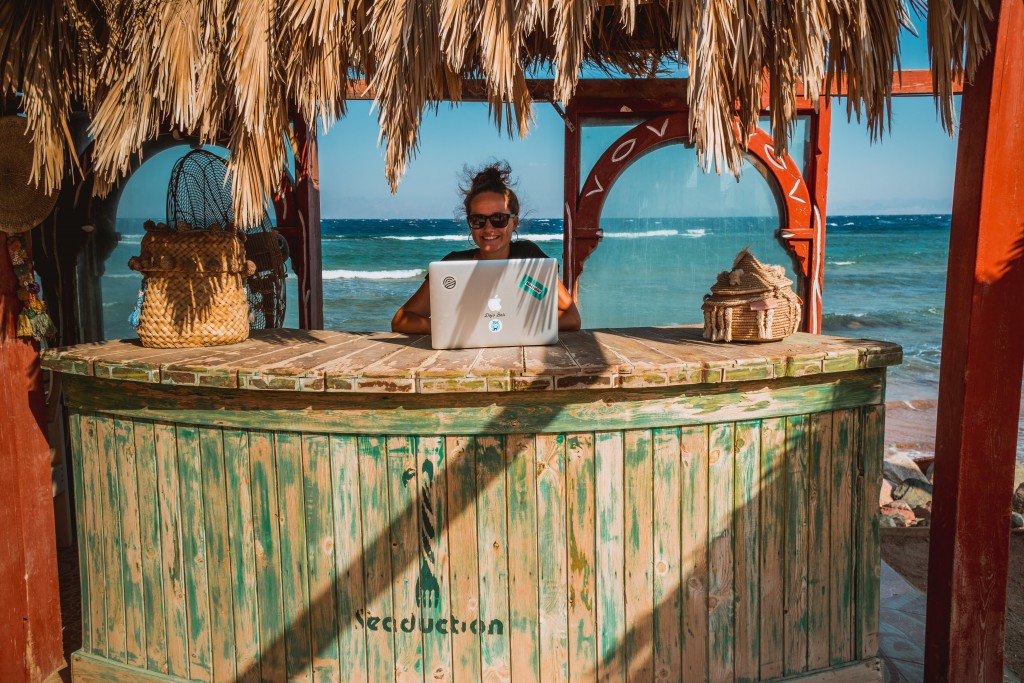 a woman works at a laptop in front of a beach scene while taking your business online