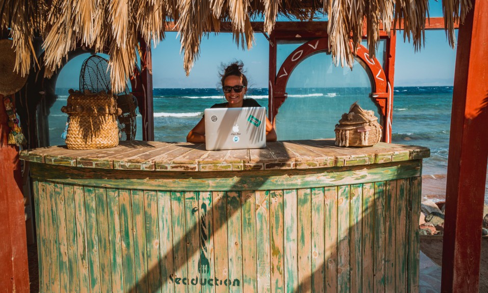 a woman works at a laptop in front of a beach scene while taking your business online