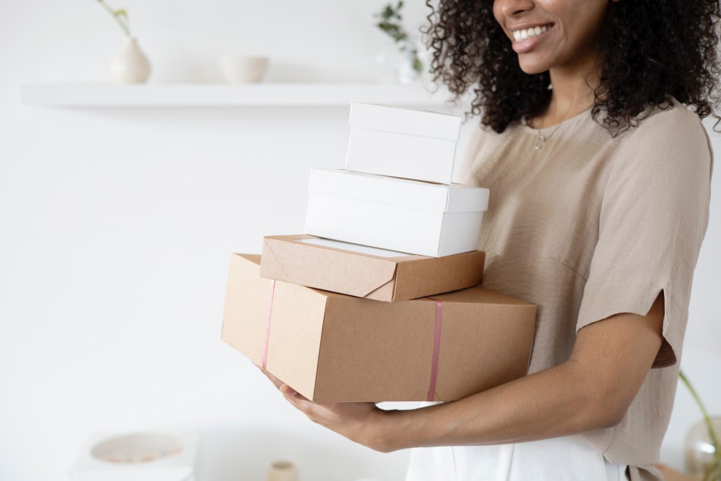 a woman smiles while holding a stack of boxes