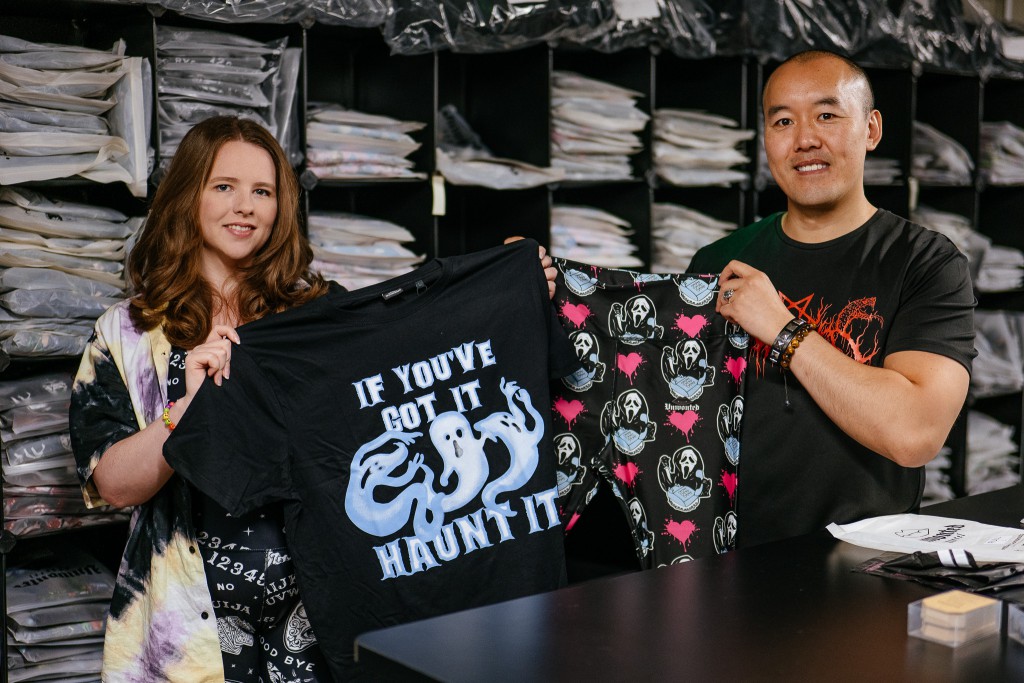 kit and lisa stand in the unwonted apparel warehouse, holding up two items from their collection