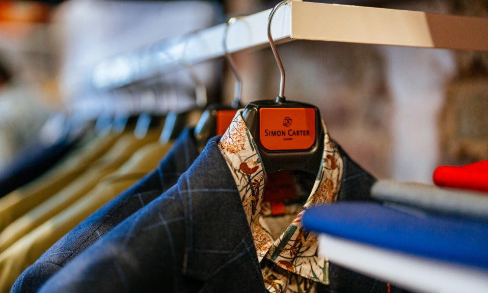 a collared shirt and suitcoat hang on a rack showing a simon carter brand on the hanger